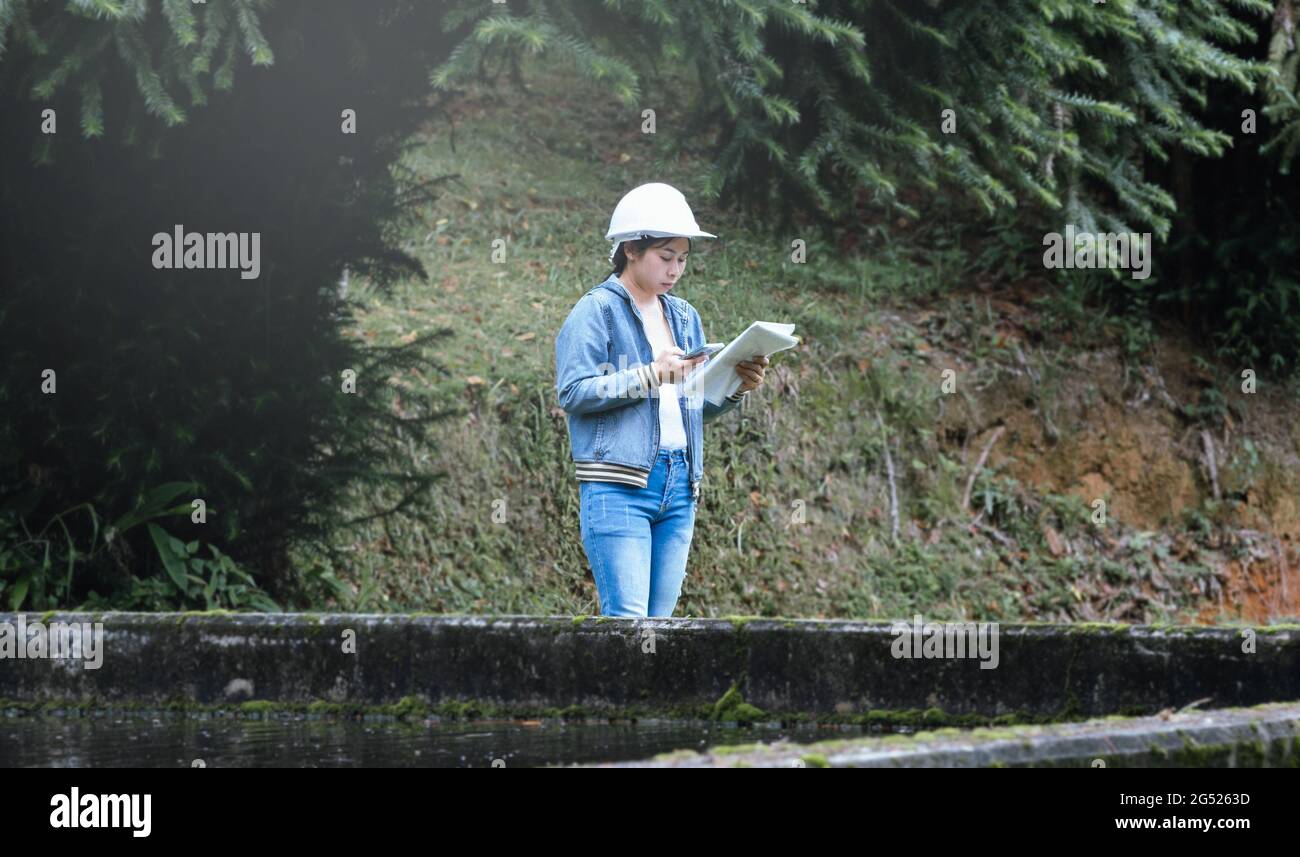 Ecologa femminile in cappelli di sicurezza che lavora e controlla una qualità dell'acqua presso l'impianto di trattamento delle acque reflue. Ingegneri ambientali che lavorano in Water recy Foto Stock