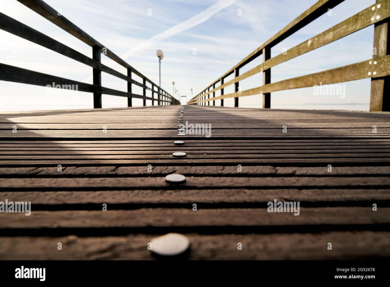 Vista dal suolo su un molo vuoto in legno con chiodi e una ringhiera, in prospettiva centrale con profondità di campo decrescente Foto Stock