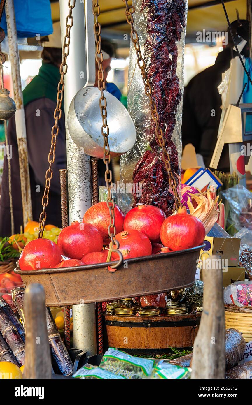 Mostra di melograni all'interno di una vecchia bilancia in metallo appesa con catene arrugginite con pomodori secchi, frutta e verdura sullo sfondo. Foto Stock