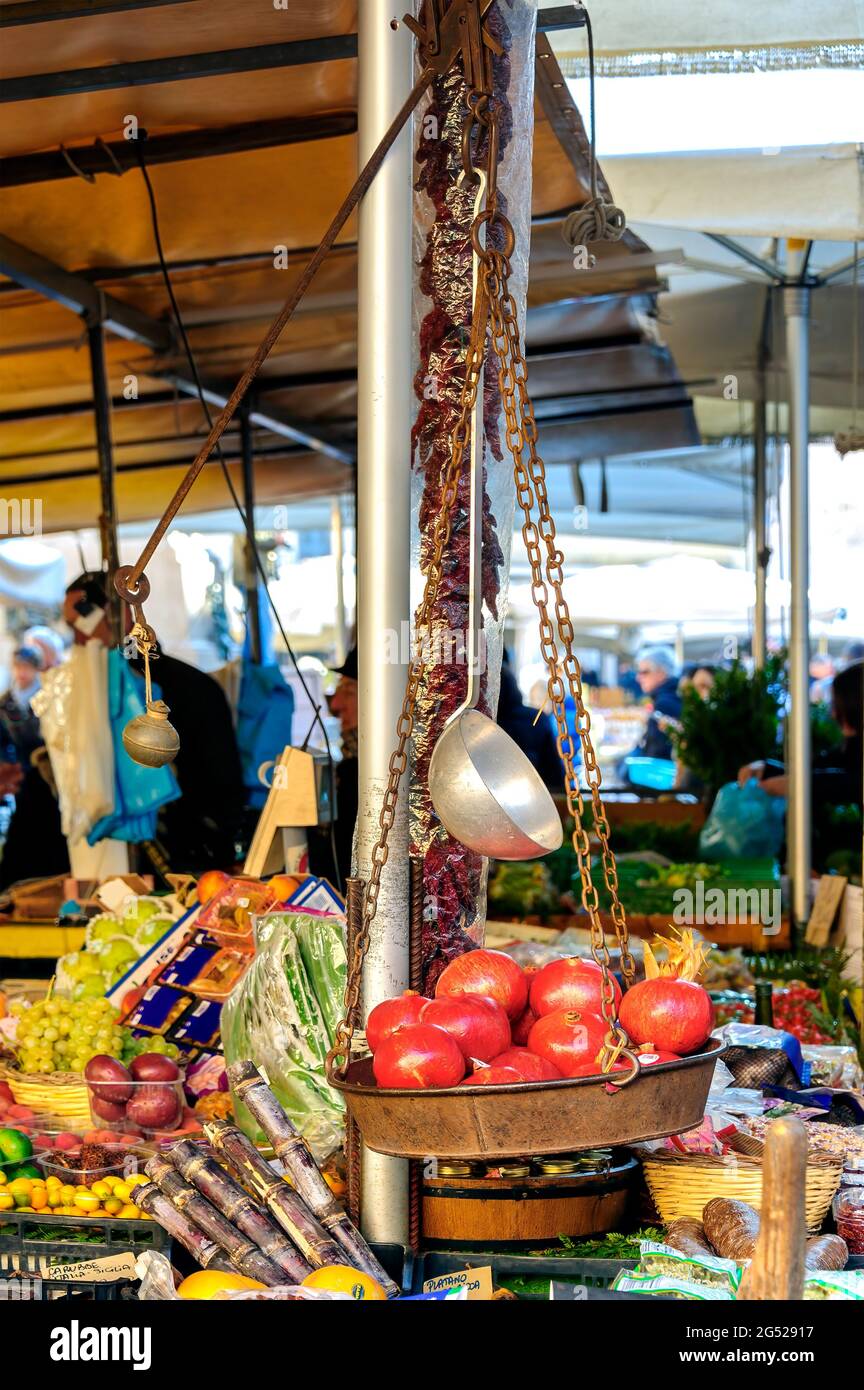 Mostra di melograni all'interno di una vecchia bilancia in metallo appesa con catene arrugginite con pomodori secchi, frutta e verdura sullo sfondo. Foto Stock