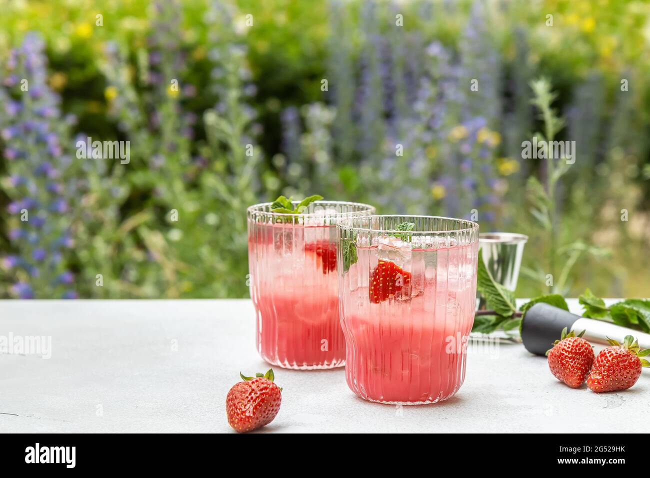 Coda di mogito fredda e fragola o cocktail con menta, cubetti di ghiaccio di fronte al giardino. Una bevanda deliziosa per dissetare la vostra sete nell'estate calda. Foto Stock