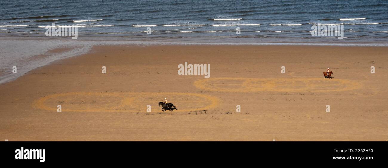 Due cavalli e cavalieri impegnati in Dressage pratica sulla spiaggia di Saltburn facendo modello classico nella sabbia. Foto Stock