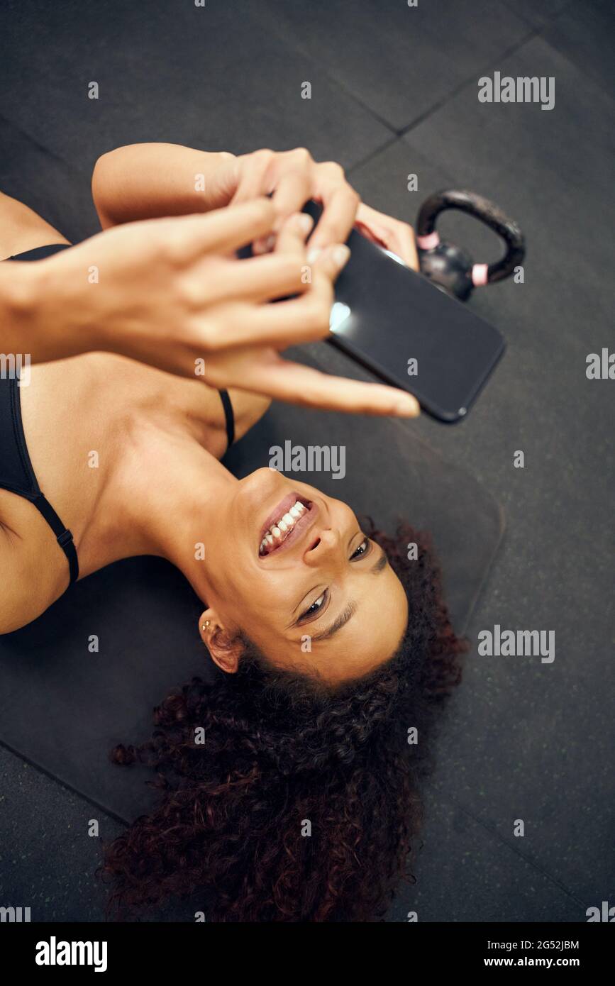 Donna afro-americana sdraiata sul pavimento e scattata una foto. Bella donna mista che sorride mentre scatta la foto. Foto di alta qualità Foto Stock