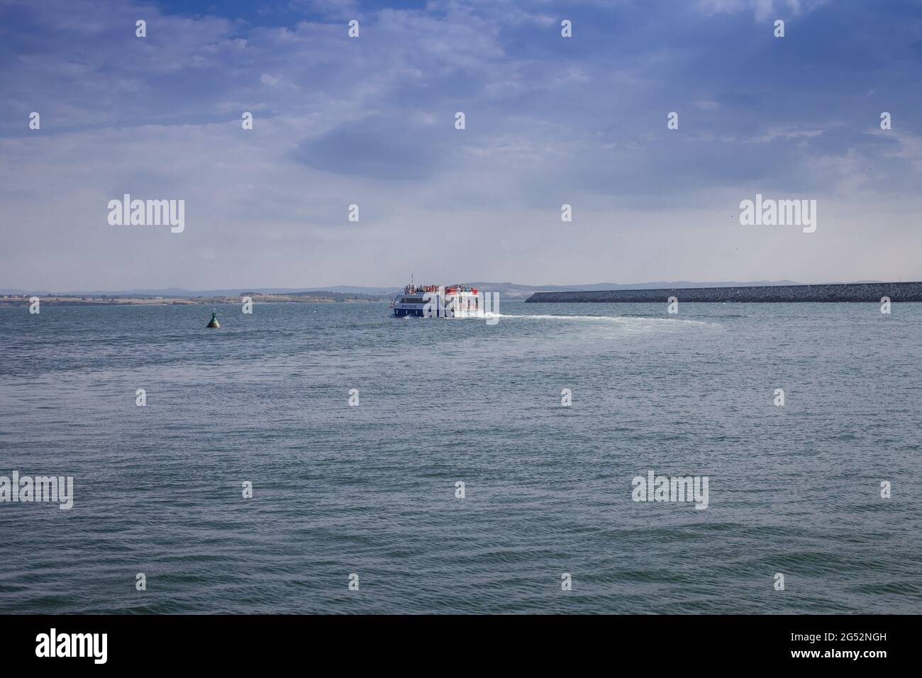 Il piccolo imbarcazione turistica da diporto 'Anastasia' salpa dal porto lungo il faro contro il cielo blu con le nuvole bianche Foto Stock