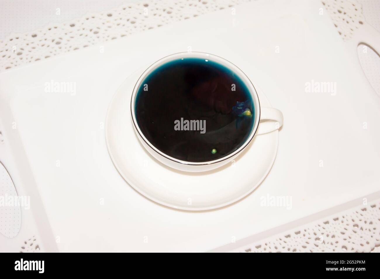 Il colore dell'umore è blu - tè blu in una tazza bianca, che si trova su un piatto bianco e un vassoio bianco bevande utili, proprietà curative. Fitoterapia. Festa del tè. Foto Stock