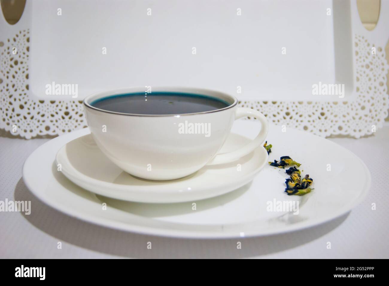 Il colore dell'umore è blu - tè blu in una tazza bianca, che si trova su un piatto bianco e un vassoio bianco bevande utili, proprietà curative. Fitoterapia. Festa del tè. Foto Stock