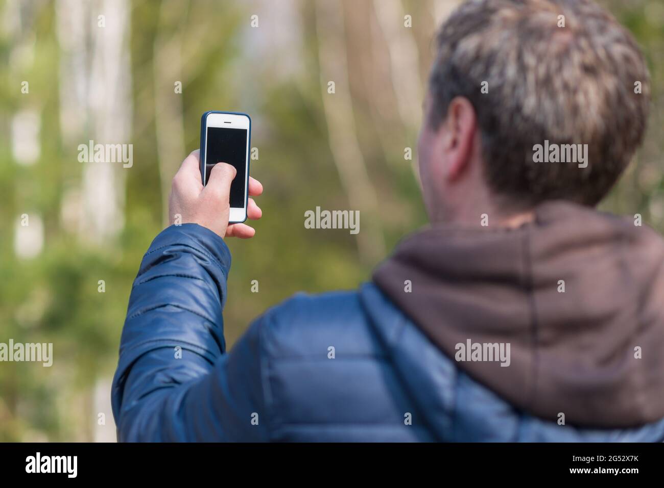 Un uomo con il suo smartphone cellulare alla ricerca del segnale di ricezione nella foresta primaverile soleggiata. Foto Stock