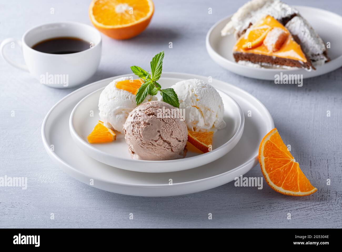 Gelato alla vaniglia e al cioccolato, torta e fette d'arancia su un tavolo di legno chiaro Foto Stock