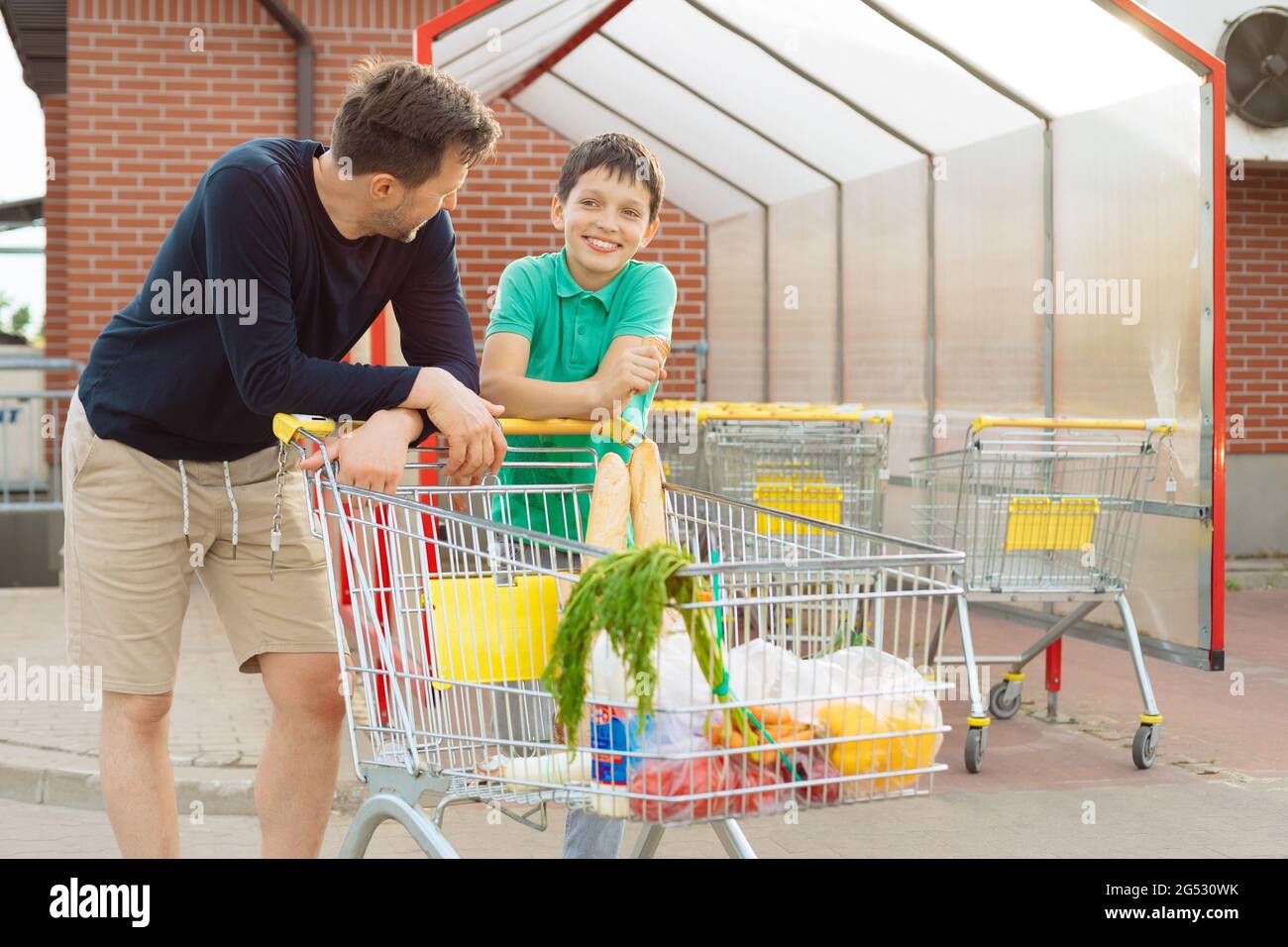 Papà e figlio hanno fatto acquisti insieme e camminare in auto con il carrello della spesa, passare il tempo insieme, le conversazioni degli uomini Foto Stock