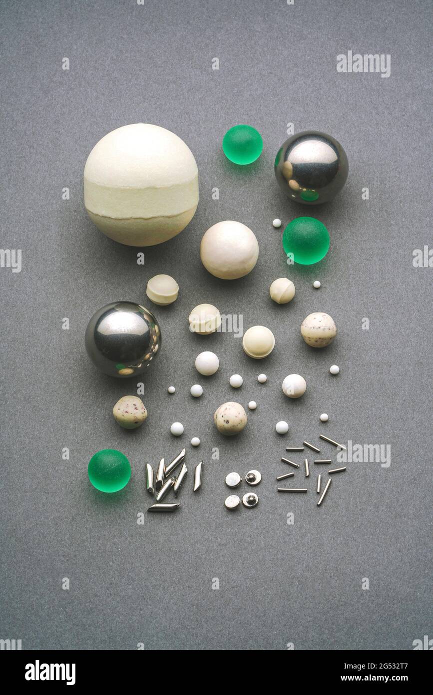 Vista dall'alto ravvicinata che mostra un gruppo di vetri industriali assortiti, sfere di ceramica e aghi utilizzati per la macinazione disposti su sfondo grigio all'interno Foto Stock
