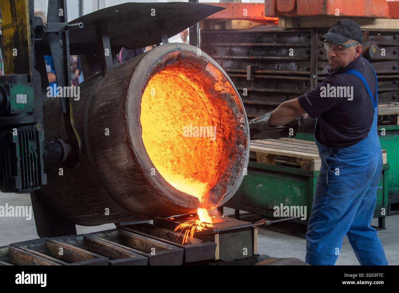 Freiberg, Germania. Giugno 25 2021: Un dipendente del Sächsisches Metallwerk di Friburgo versa un campione di metallo del fuso per una campana per la Cattedrale di Merseburg in una muffa. L'occasione per il lancio della campana è il 1000° anniversario della consacrazione della cattedrale di quest'anno. La campana peserà 890 chilogrammi e suonerà in un unico G. il tono si armonizzerà con le altre campane della cattedrale. Il tono si armonizza con le due grandi campane della chiesa. La campana sarà consacrata il 1° ottobre. La fusione è stata resa possibile da una sovvenzione di 50,000 euro della Friede Springer Foundation. In rosso Foto Stock