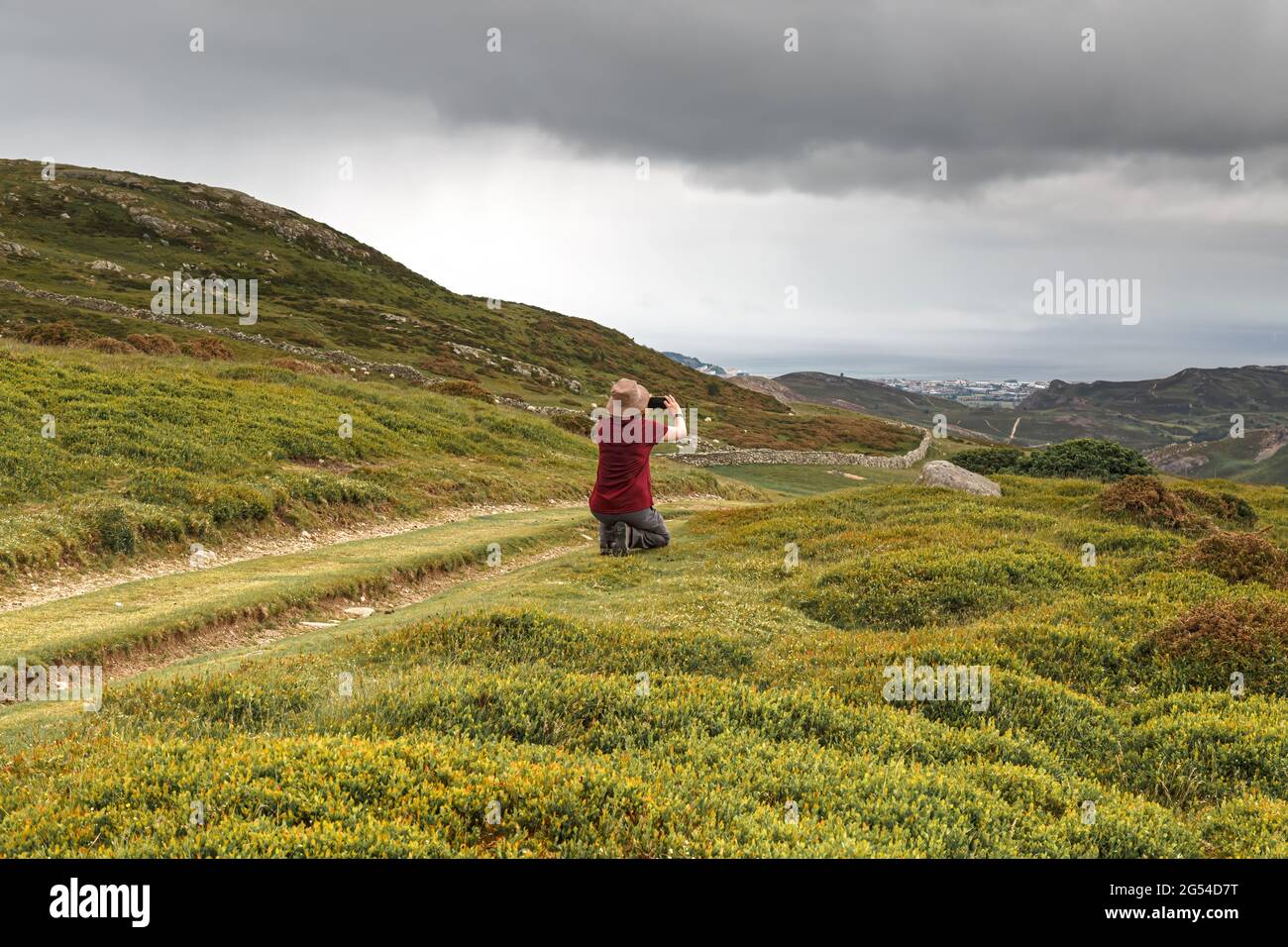 Una sola donna che scatta fotografie utilizzando un telefono cellulare sul paesaggio del percorso costiero del Galles a Penmaenmawr, Cony, Galles Foto Stock