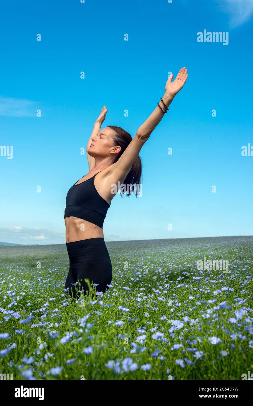 Donna sportiva con le braccia sollevate che si allungano in un campo con cielo blu. Foto Stock