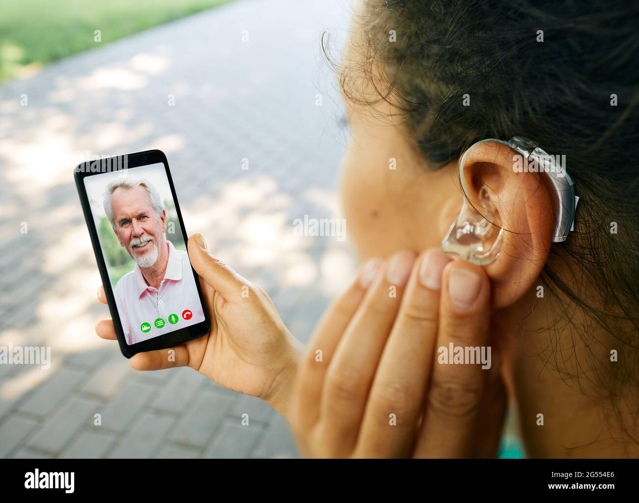 La donna adulta con un apparecchio acustico nell'orecchio comunica con il padre tramite comunicazione video tramite smartphone. Vita umana completa con apparecchi acustici Foto Stock