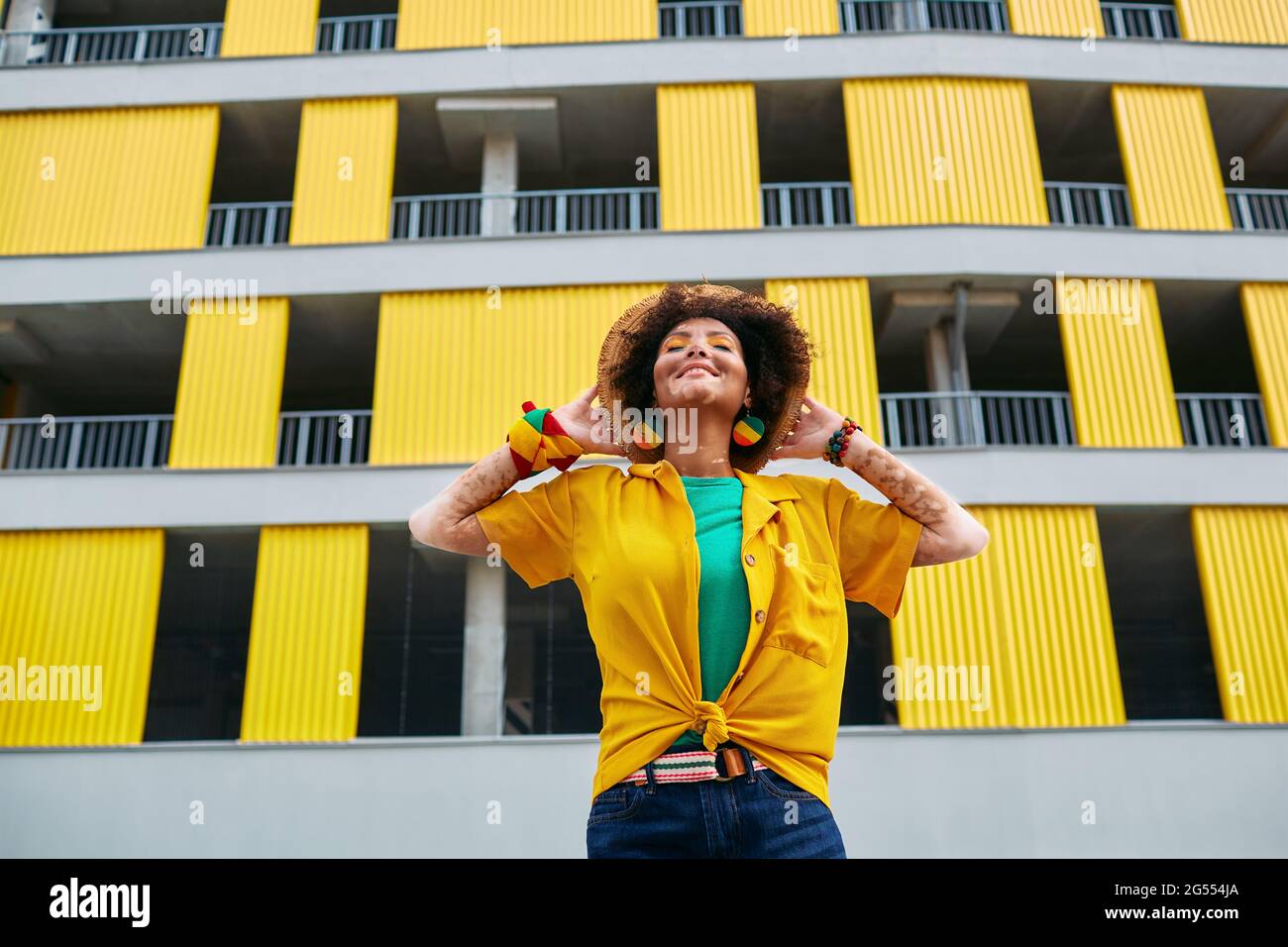 Donna hipster felice con vitiligo godendo la vita mentre si trova sullo sfondo di un edificio urbano grigio-giallo. Godetevi la vita della città Foto Stock
