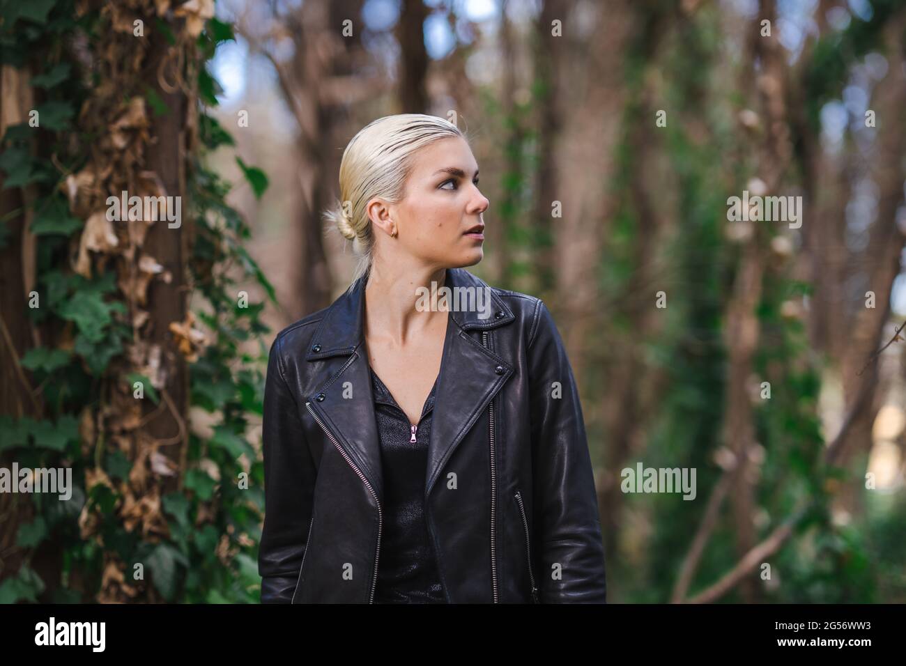 Moda in luoghi insoliti, giovane donna in giacca Edgy Moto nella foresta Foto Stock