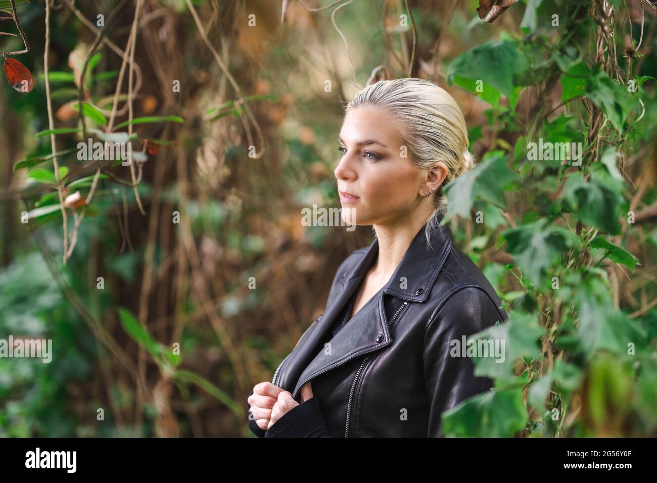 Moda in luoghi insoliti, giovane donna in giacca Edgy Moto nella foresta Foto Stock