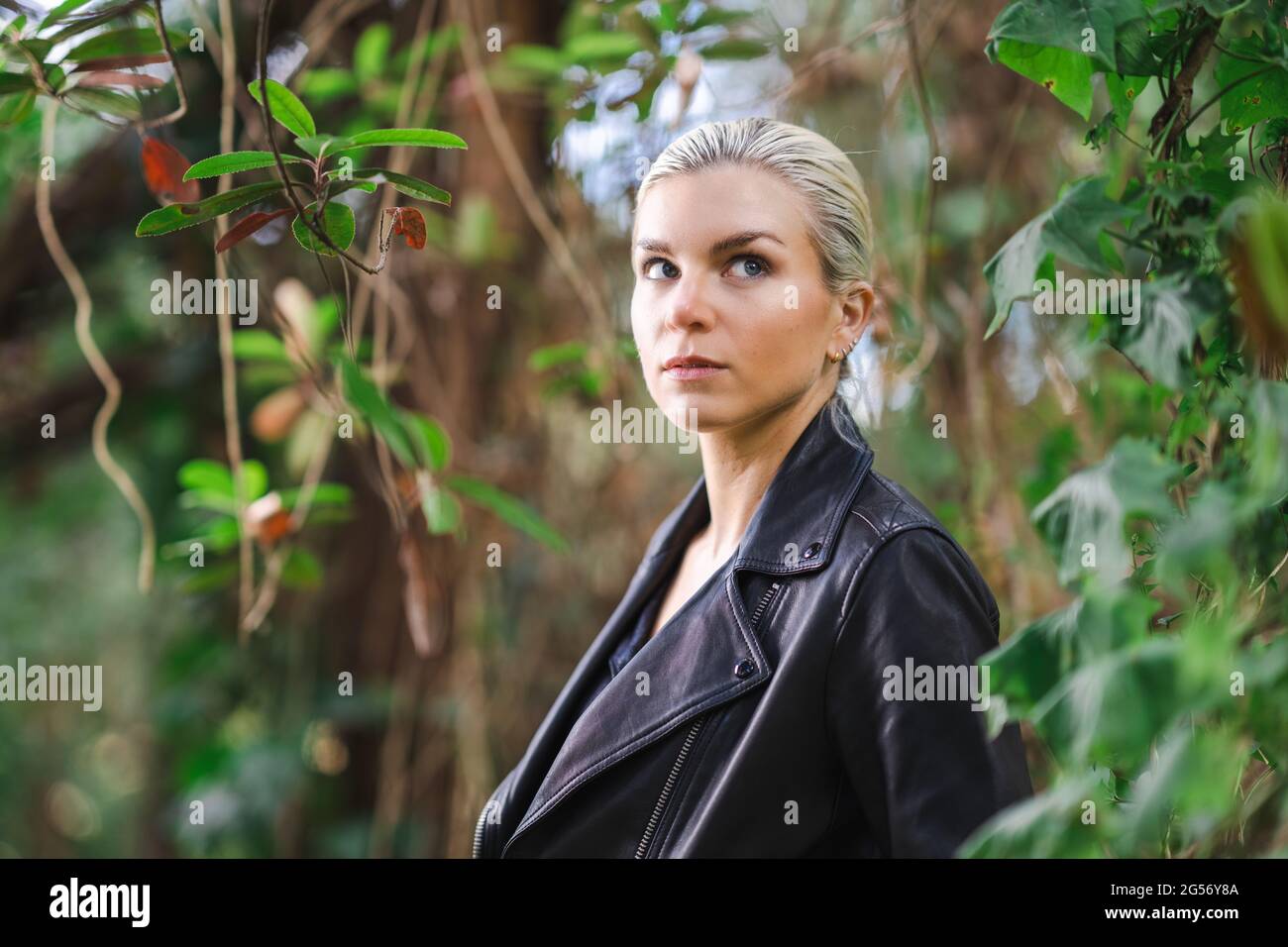 Moda in luoghi insoliti, giovane donna in giacca Edgy Moto nella foresta Foto Stock