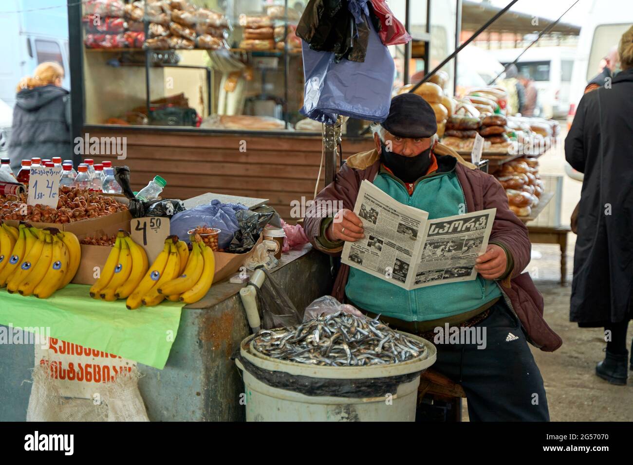 Uomo georgiano sovrappeso. Un venditore del mercato di strada legge un giornale mentre si siede al banco. Foto Stock