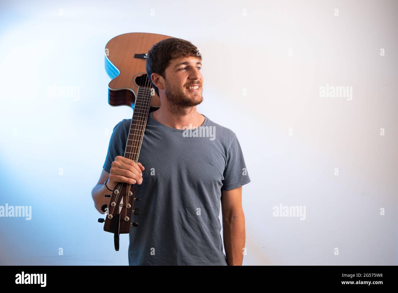 Un musicista sorridente con la chitarra appoggiata sulla spalla, guarda a destra. studio foto con sfondo bianco Foto Stock