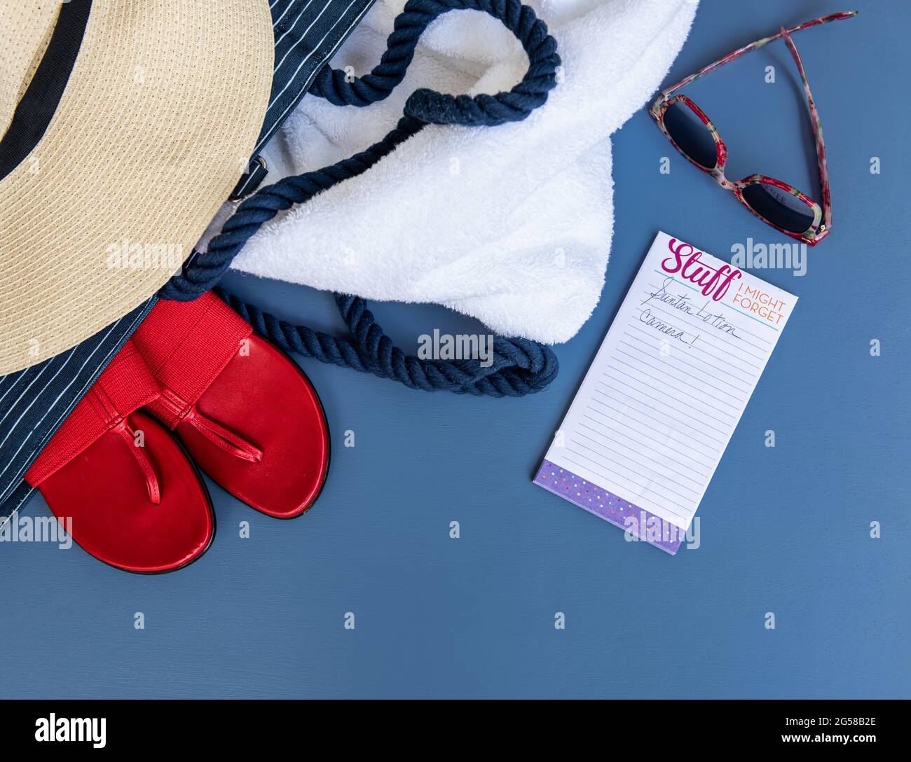 Posato piatto di beachwear con un cappello, scarpe, occhiali da sole e una lista. Foto Stock