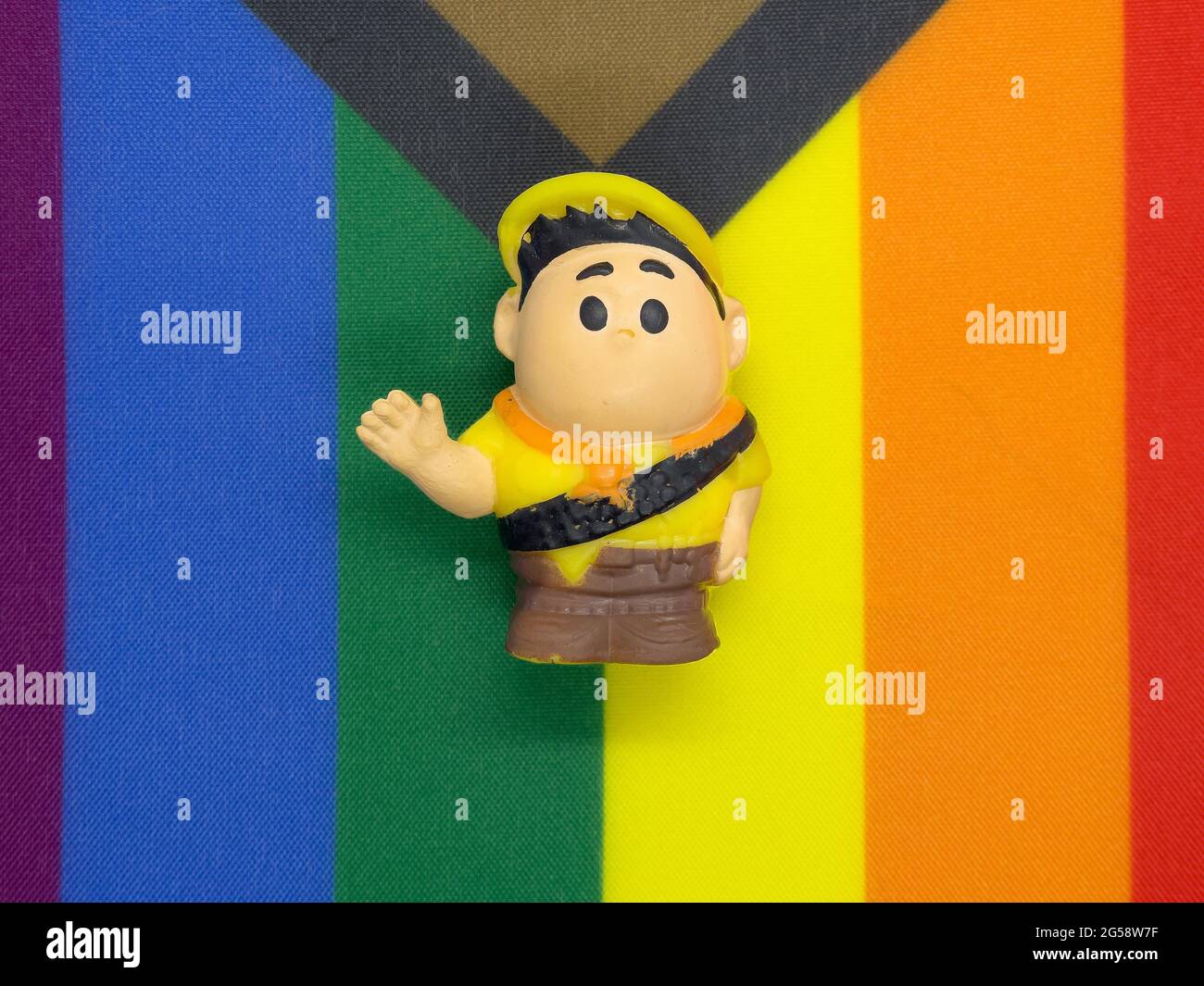Il ragazzo giocattolo alza la mano e si sdraia sulla bandiera dell'orgoglio arcobaleno Foto Stock
