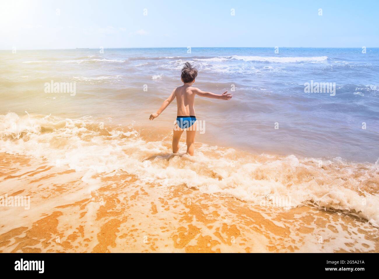 Carino ragazzino che corre attraverso l'acqua in spiaggia, il bambino entra l'onda del mare, vacanza estiva Foto Stock