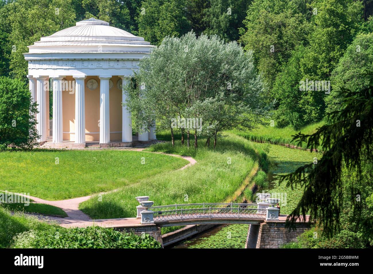 un tempio in stile classico in uno splendido parco estivo. Campo verde con dandelioni bianchi e gialli all'aperto natura in estate. Campo estivo verde luminoso Foto Stock