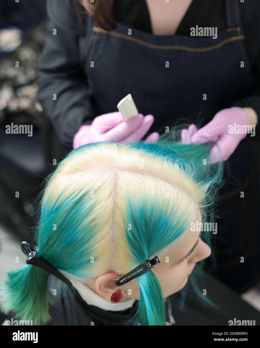 Vista dall'alto della testa della giovane donna con capelli verdi, radici dei capelli sbiancate, separazione dei capelli. Donna in salone di bellezza professionale prima del processo di colorazione dei capelli Foto Stock