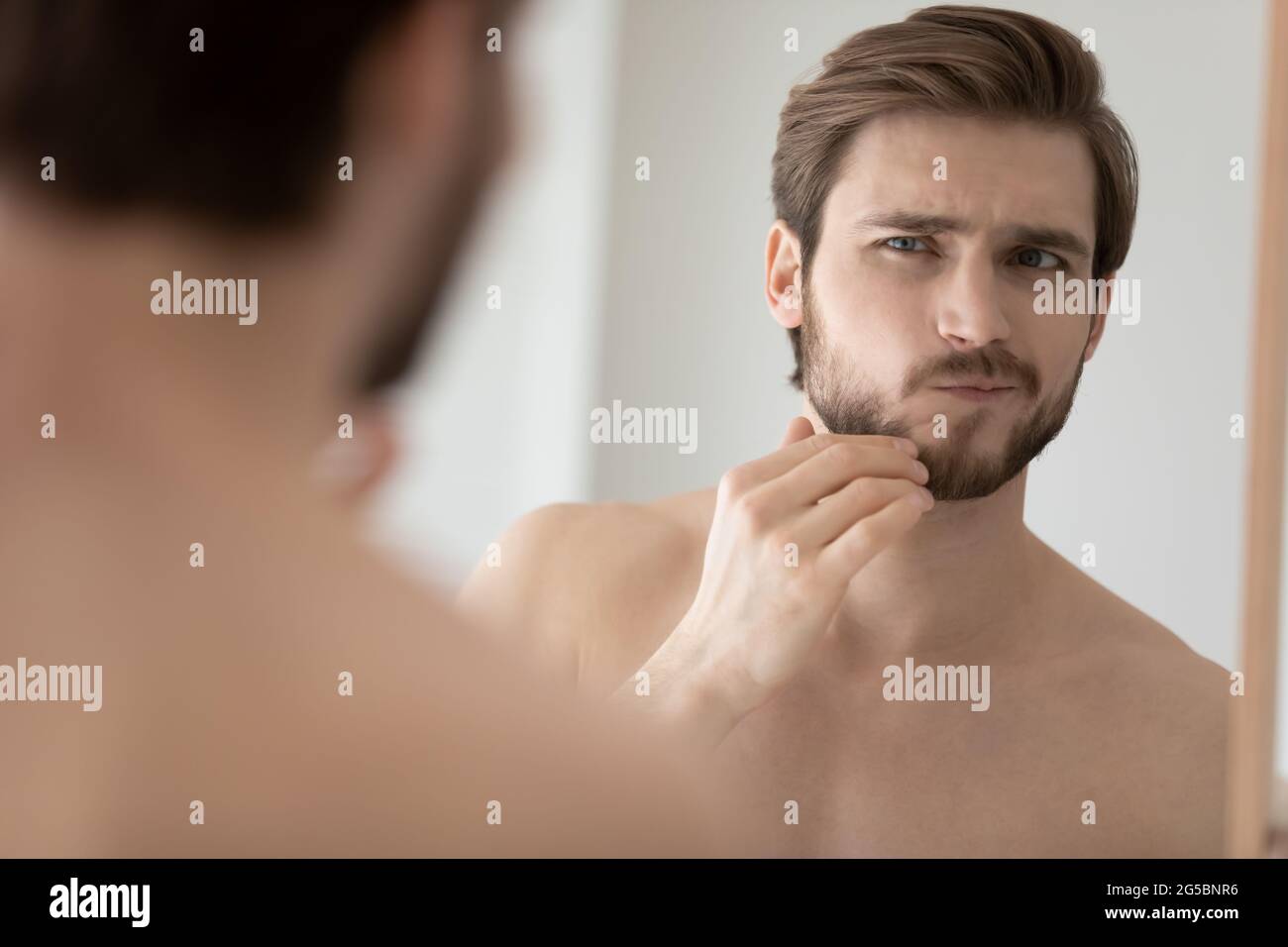 Preoccupatevi giovane bell'uomo che esamina il volto in riflessione speculare Foto Stock