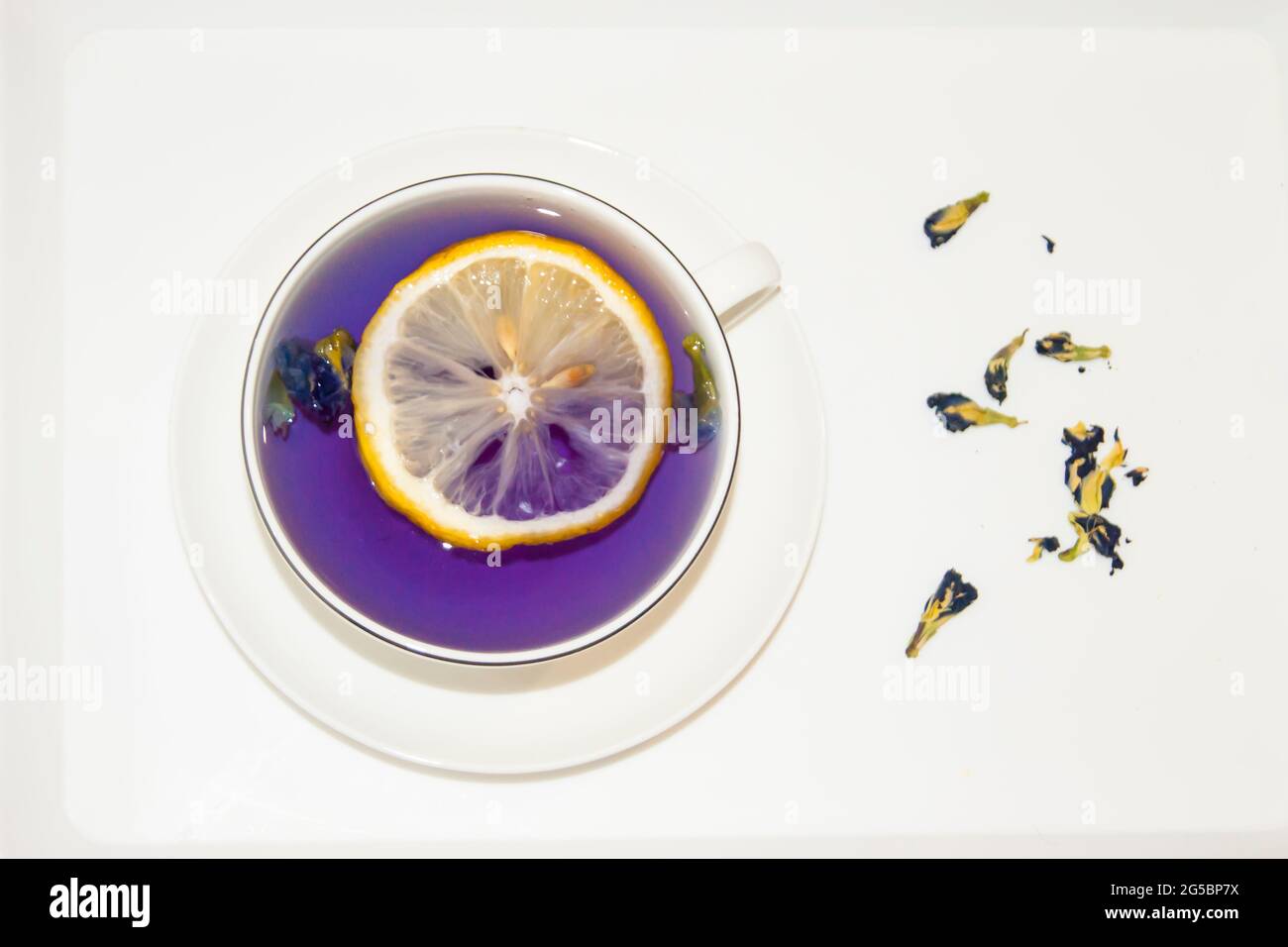 Il colore dell'umore è blu - tè blu con limone in una tazza bianca, che si trova su un piatto bianco e vassoio bianco contrasto. Bevande utili, proprietà curative. Fitoterapia. Festa del tè. Foto Stock
