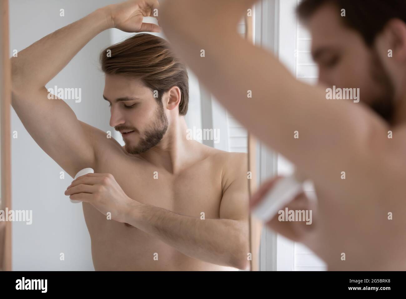 Calmo bel giovane uomo ben costruito con deodorante Foto Stock