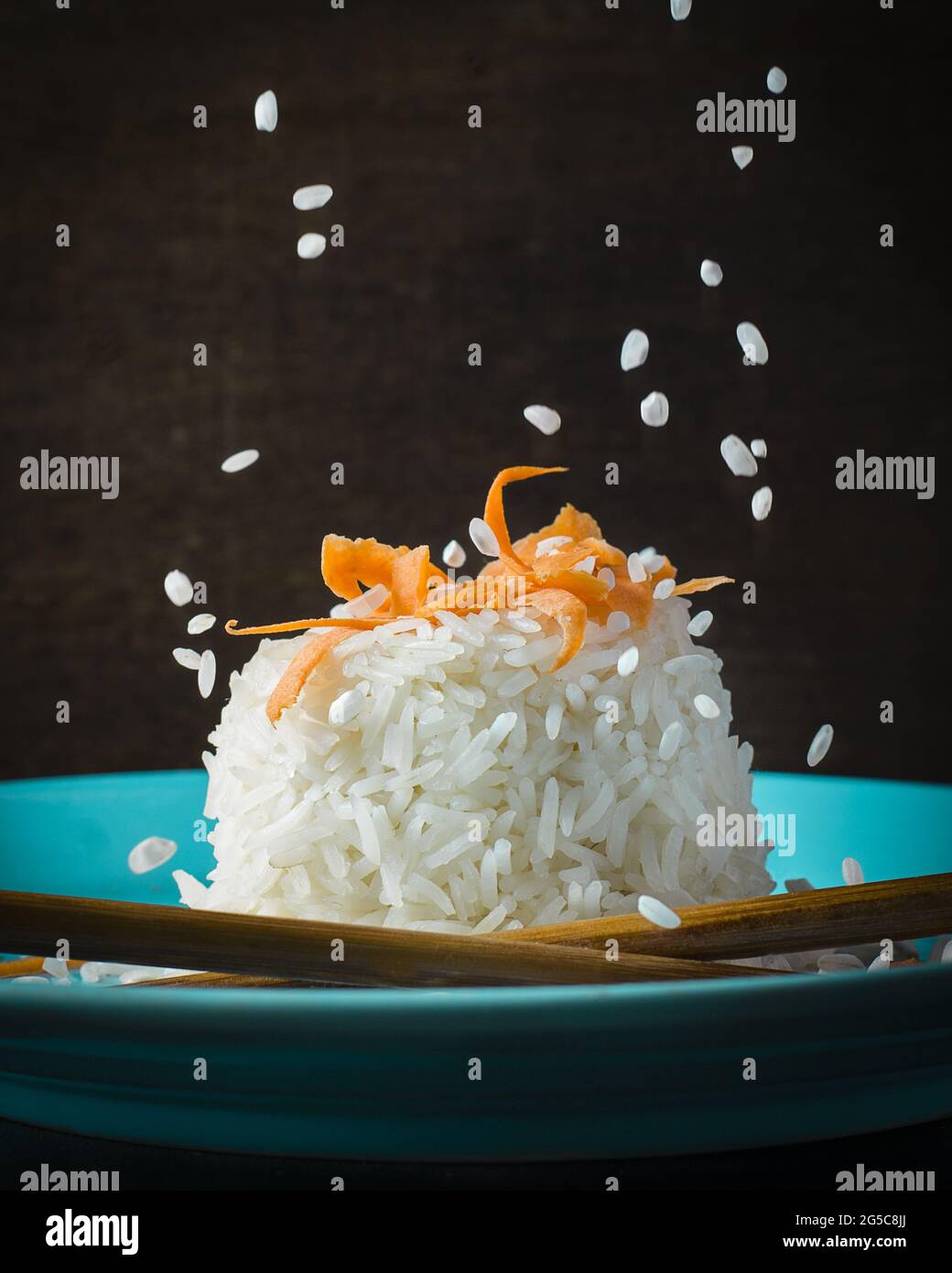 Colpo verticale di riso con la parte superiore della carota in un piatto blu e sfondo scuro Foto Stock