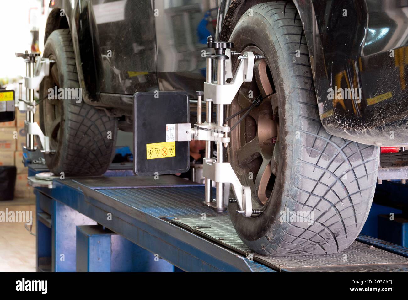 Pneumatico dell'auto bloccato con aligner sottoposto a regolazione automatica dell'angolo delle ruote, allineamento e bilanciamento delle ruote nella stazione di servizio di riparazione presso il garage. Foto Stock