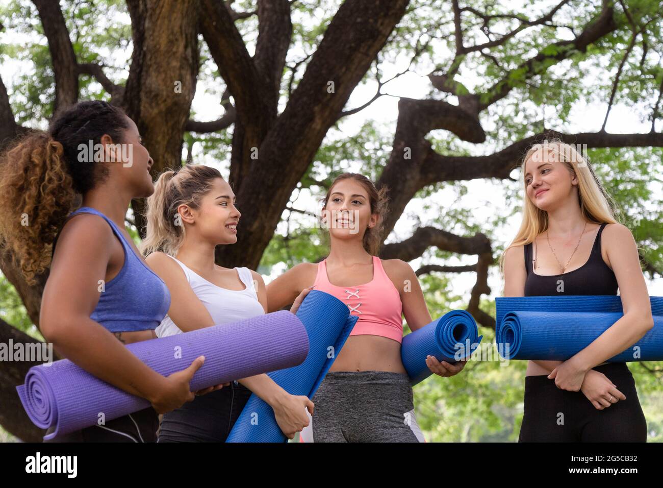 felici giovani donne multietniche amici gruppo di amici rilassarsi e parlare dopo l'esercizio di yoga nel parco al fine settimana mattina. vita dopo covid. Foto Stock