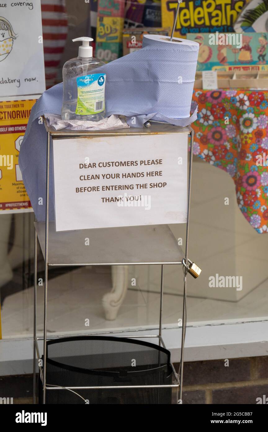 Una stazione di igienizzazione all'esterno di un negozio nel centro città con igienizzatore a pompa manuale e rotolo di carta blu e un cartello da utilizzare prima di entrare in negozio Foto Stock