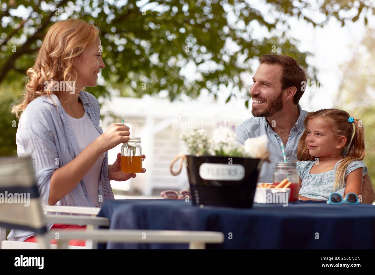 i genitori caucasici si guardano a vicenda, sorridendo, bevendo succo di paglia, con la bambina in grembo di papà Foto Stock