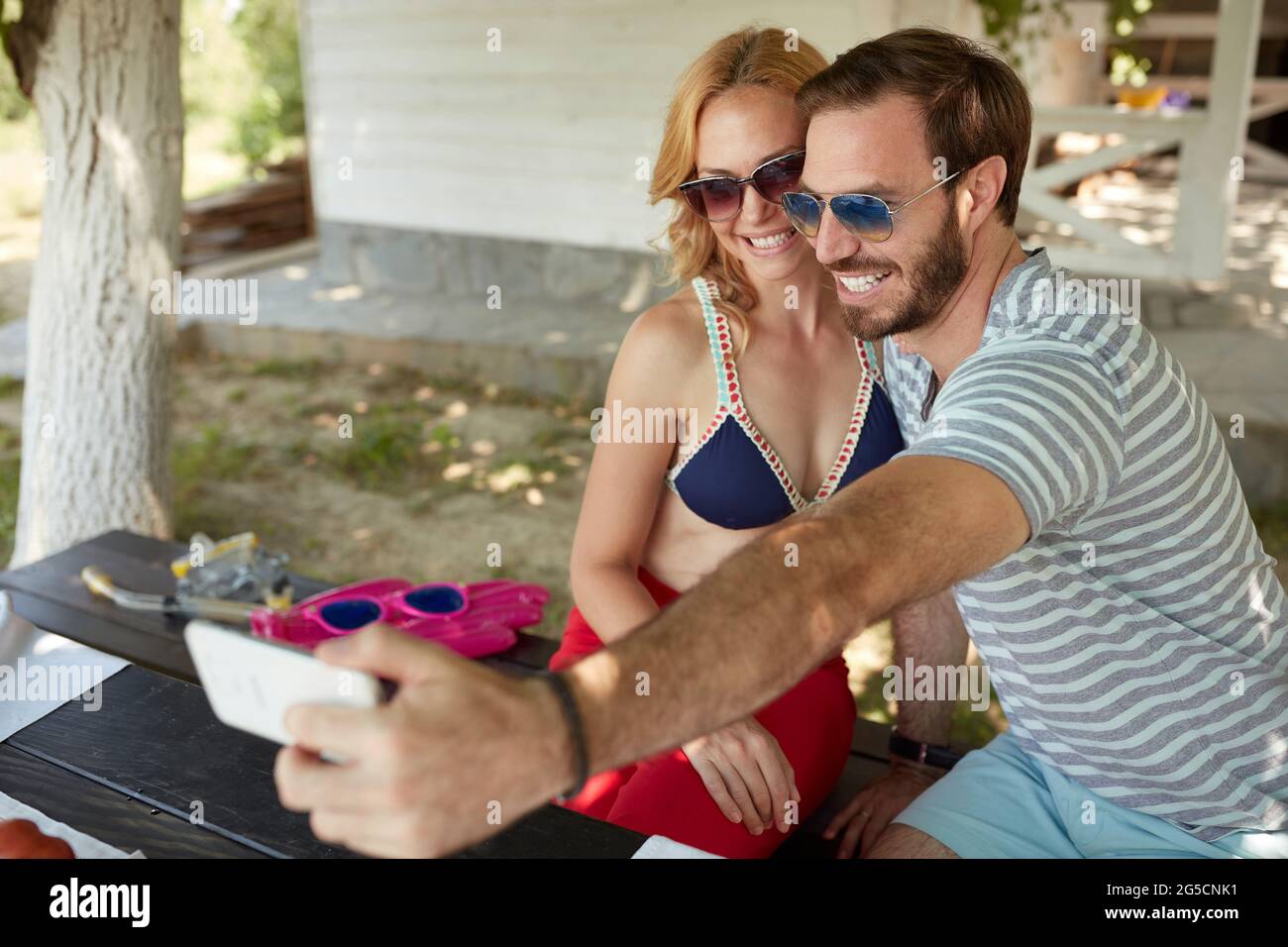 giovane coppia adulta caucasica che prende selfie, seduto su una panchina nel cortile, sorridente Foto Stock