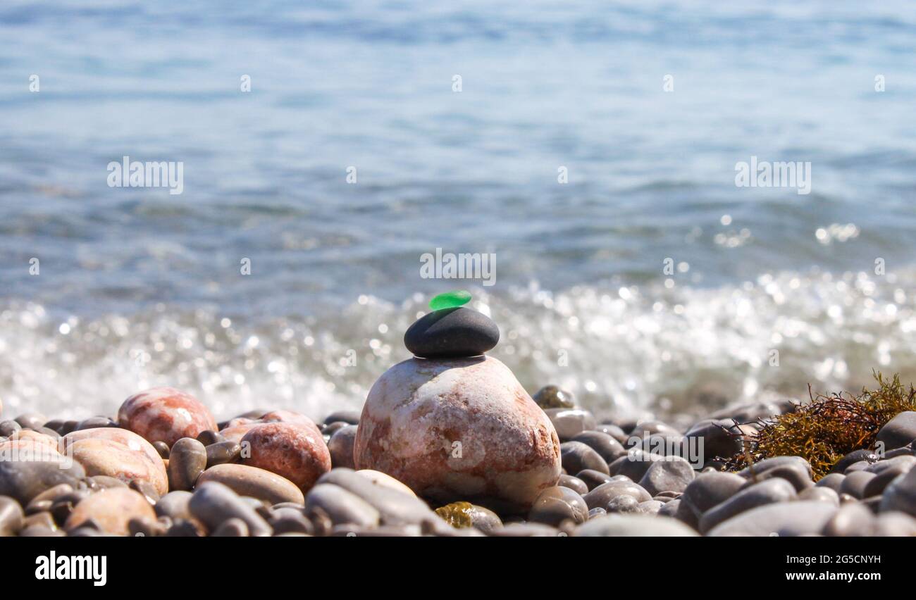 La piramide è costruita su una spiaggia di ciottoli di mare con un vetro verde satinato liscio in cima. Sullo sfondo di onde, schizzi d'acqua e. Foto Stock