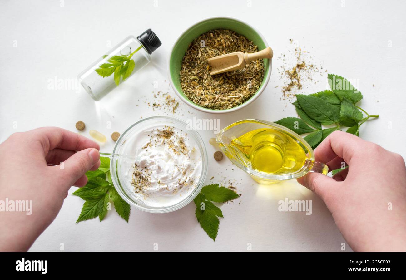 Preparazione di una medicina alternativa, estratto di erbe: Fondo bianco, mani tenere un vaso di olio su una ciotola con essenza bianca, e mescolando. Ciotola con g Foto Stock
