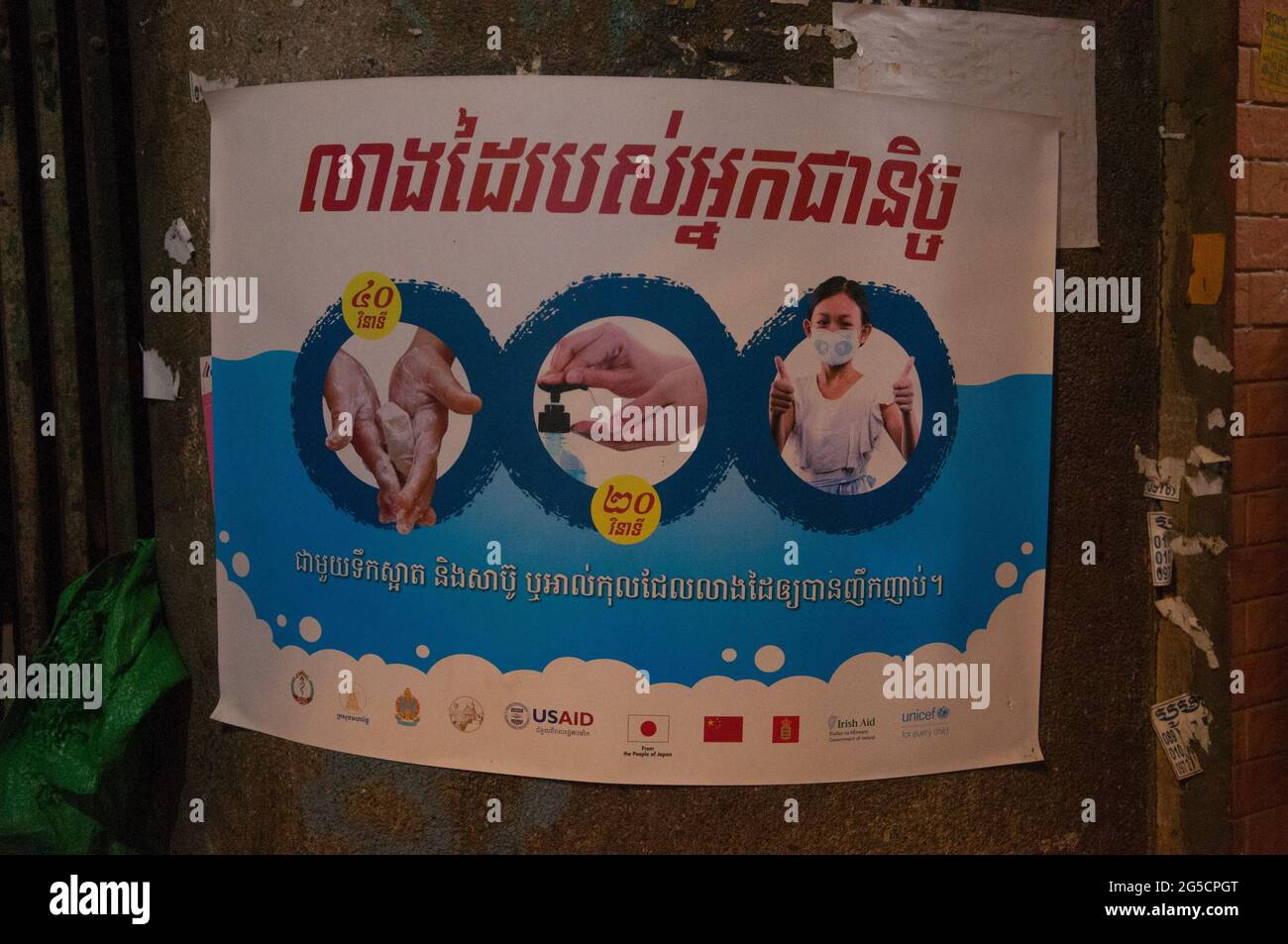 Durante uno scoppio di COVID - 19, USAID mette in su i manifesti in scritto di Khmer che avvertono la gente per lavare le loro mani, usare l'igienizzatore della mano & indossare le maschere del viso, in una baraccopoli vicino al mercato di Kandal, durante la pandemia del coronavirus. Phnom Penh, Cambogia. 22 febbraio 2021. © Kraig Lieb Foto Stock