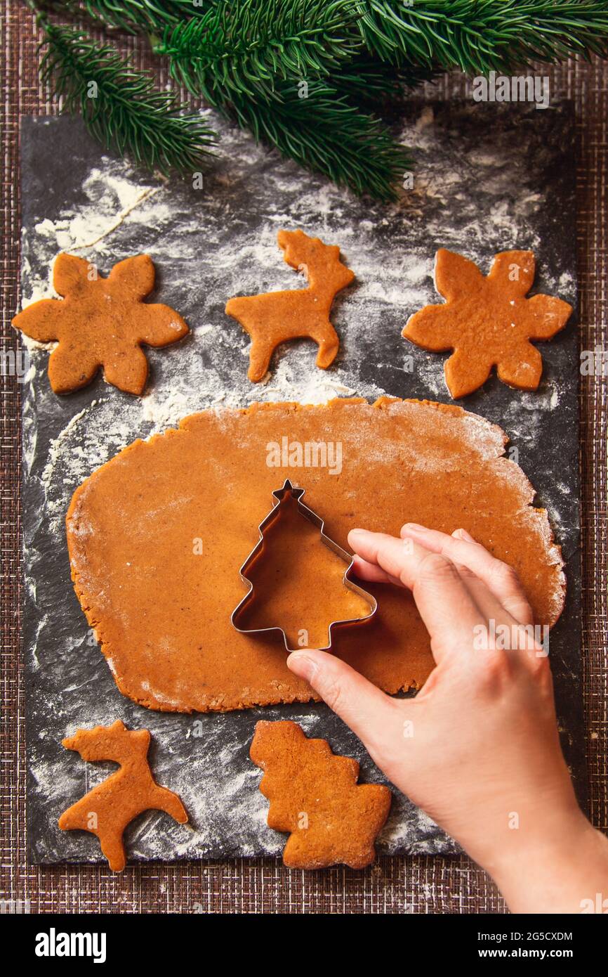Il processo di fabbricazione dei biscotti dello zenzero di Natale. La donna tiene la muffa a forma di albero di Natale su pasta cruda per i biscotti di zenzero. Foto Stock