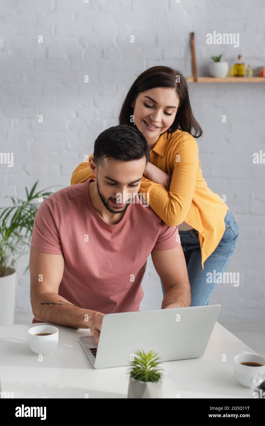 giovane coppia positiva in abiti casual guardando il computer portatile a casa Foto Stock