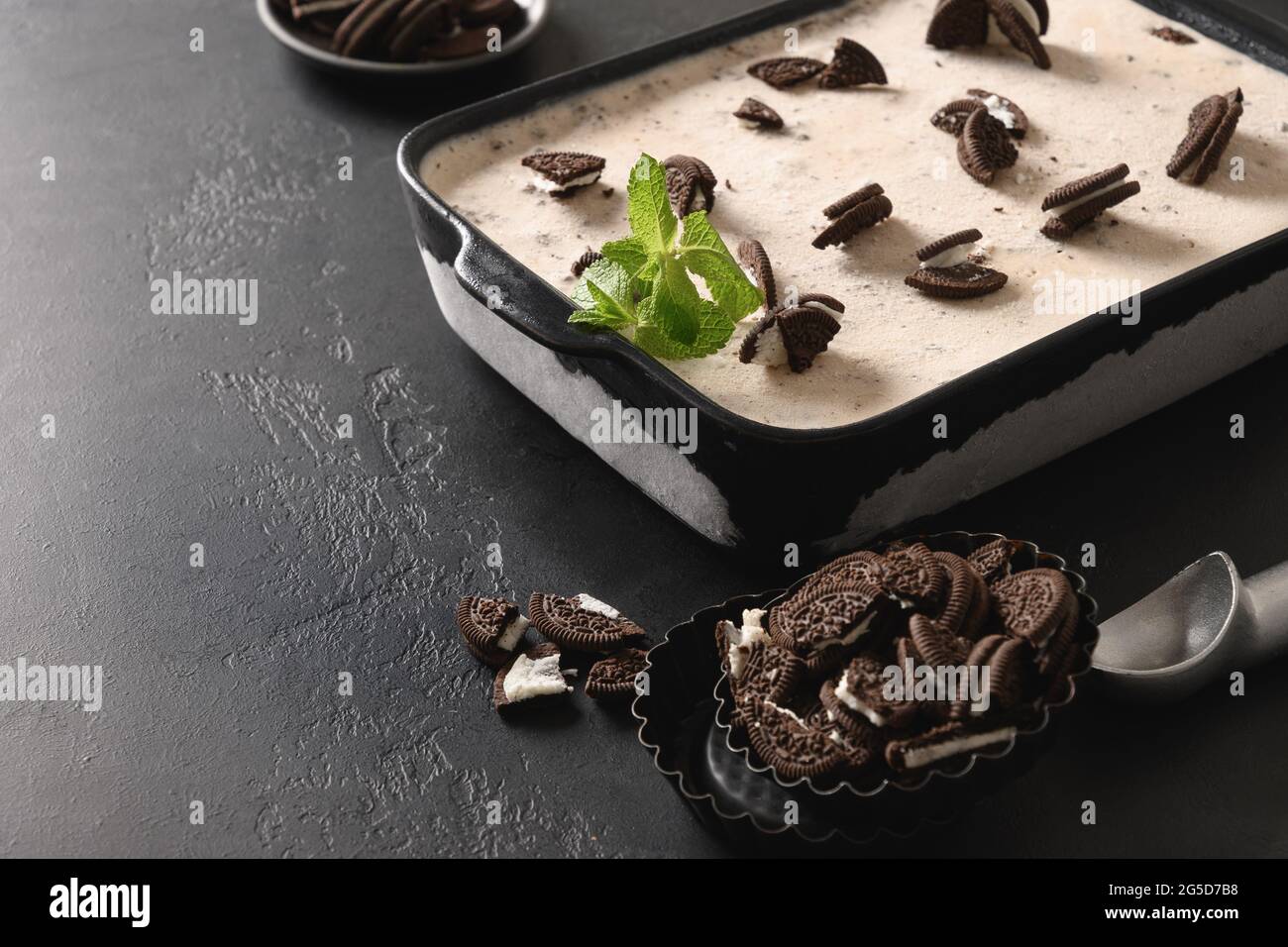 Gelato cremoso fatto in casa con biscotti al caffè in contenitore su sfondo nero con spazio copia. Primo piano. Gustoso dessert per bambini senza zucchero. Foto Stock