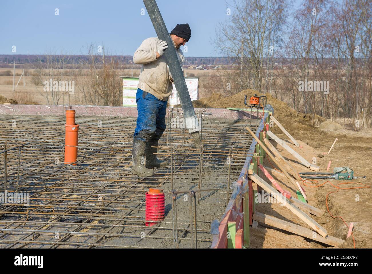 REGIONE DI LENINGRAD, RUSSIA - 28 MARZO 2021: Un lavoratore ospite versa la fondazione di una casa di campagna in costruzione Foto Stock