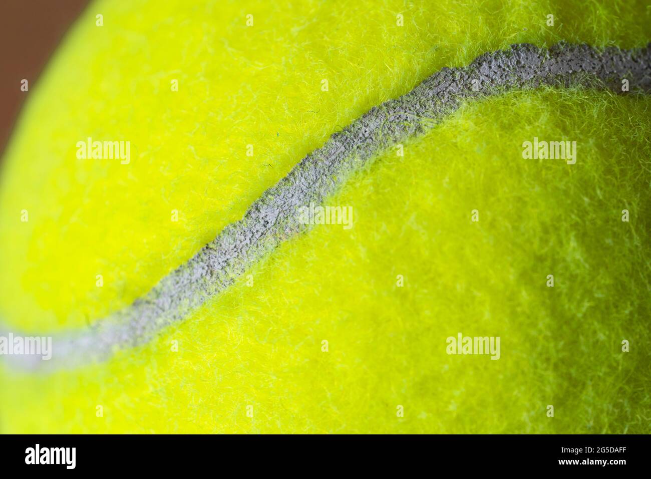 Macro closeup di una palla da tennis gialla fluorescente (giallo ottico) che mostra la copertura in feltro fibroso e l'ovale curvilineo bianco Foto Stock
