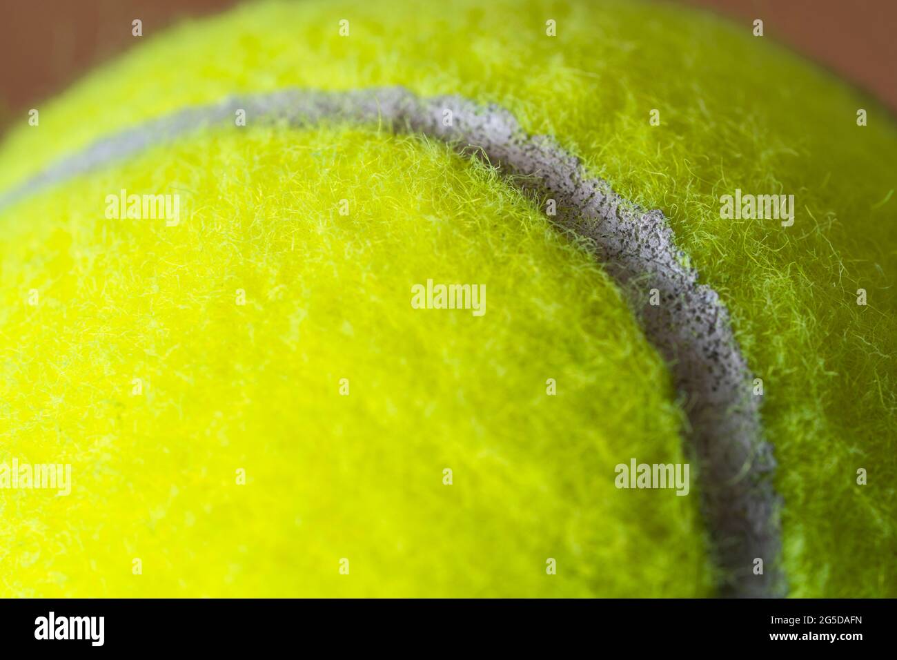 Macro closeup di una palla da tennis gialla fluorescente (giallo ottico) che mostra la copertura in feltro fibroso e l'ovale curvilineo bianco Foto Stock