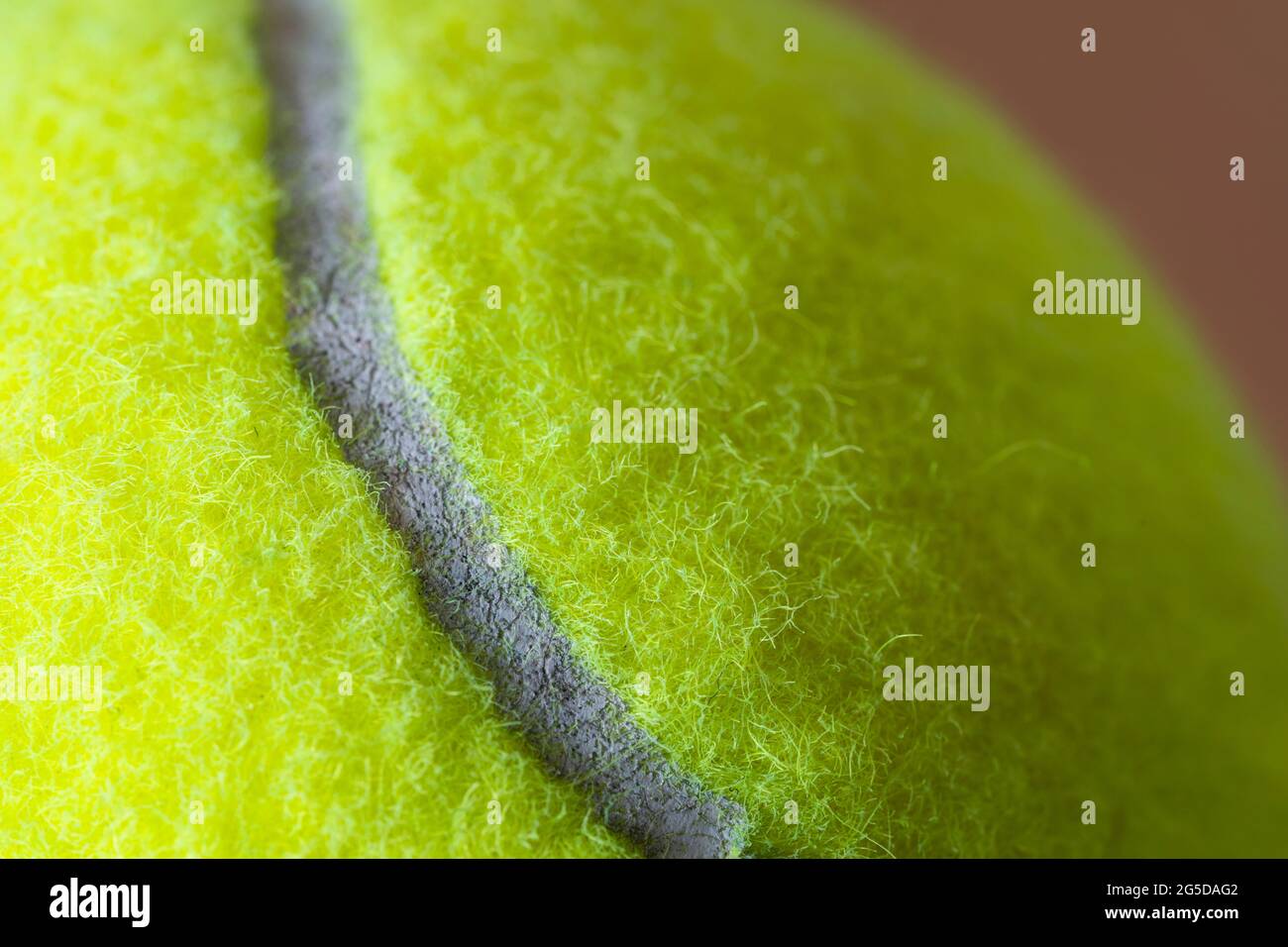 Macro closeup di una palla da tennis gialla fluorescente (giallo ottico) che mostra la copertura in feltro fibroso e l'ovale curvilineo bianco Foto Stock