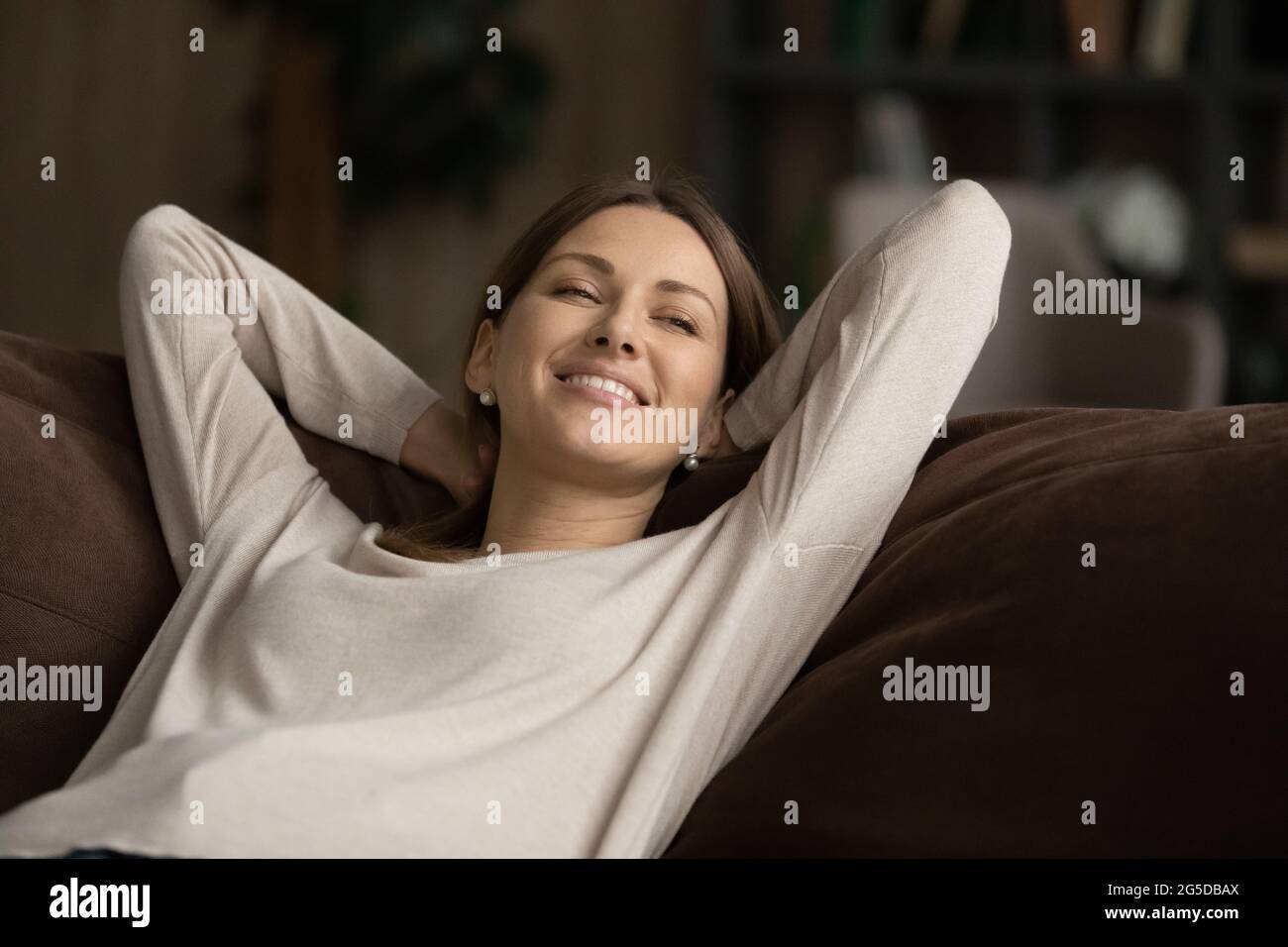 Sorridente attraente generazione millenaria donna che si rilassa su un comodo divano. Foto Stock