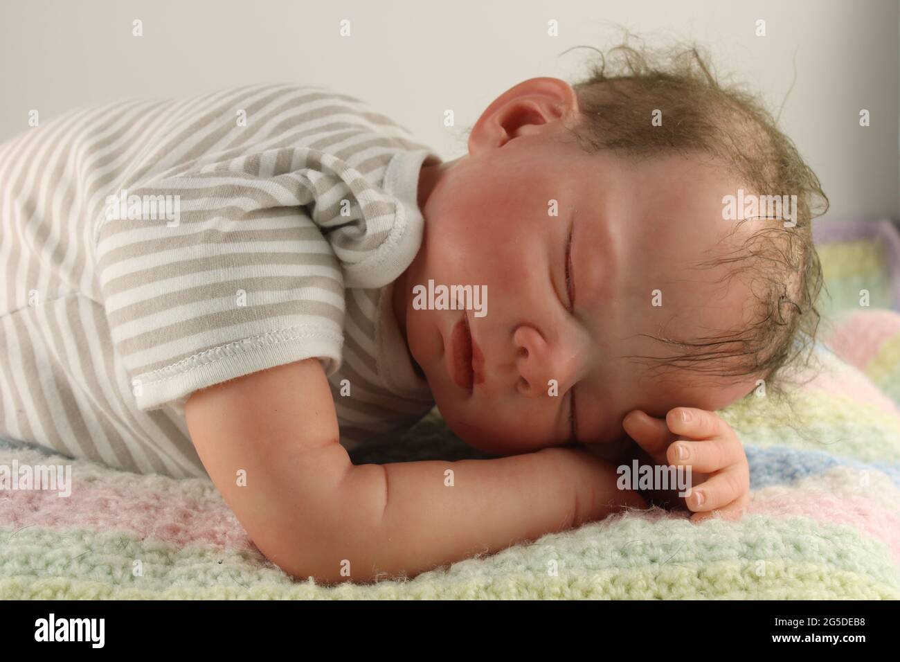 Bambino addormentato sdraiato su una coperta di maglia, concetto di Parenthood rappresentato da una bambola rinascita Foto Stock